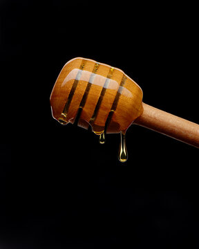 Liquid honey dripping from wooden spoon on black background