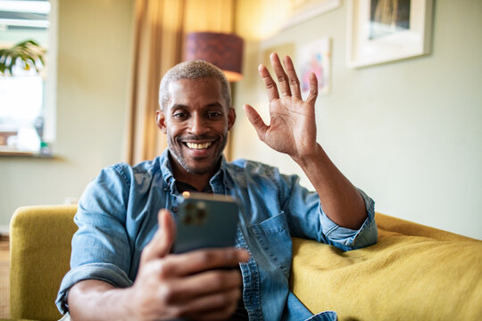 Middle aged man greeting his friend on a smartphone video call at home
