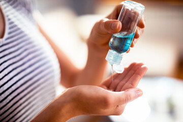 Close up view of a young woman using a small portable antibacterial hand sanitizer on hands