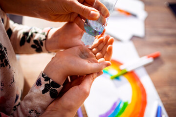 Young mother helping her daughter clean his hands with a antibacterial hand sanitizer at home