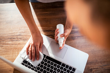 Young woman disinfecting the keyboard of her laptop at home