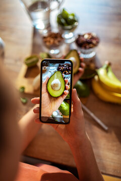 Young woman taking a picture on smartphone of healthy ingredients in the kitchen