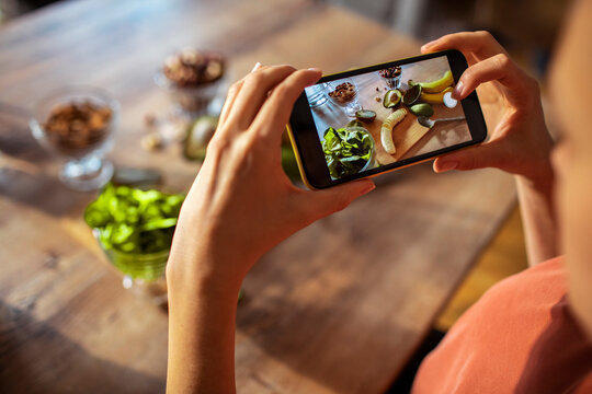 Young woman taking a picture on smartphone of healthy ingredients in the kitchen