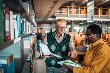 Academic advisor helping a young African American student on a paper in a college library