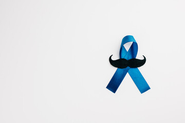 A blue ribbon with a mustache, symbolizing support for men's health, rests on a white background....