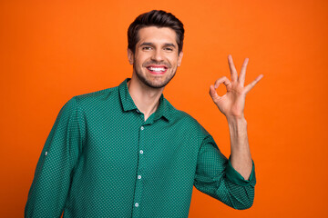 Photo of good mood funky man dressed green shirt showing okey gesture isolated orange color...