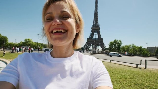 Close up of Woman is taking selfie using smartphone sitting near Eiffel tower in Paris in daytime,