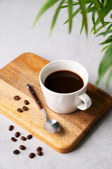 A cup of black aromatic coffee on a wooden board on a light background with coffee beans, spoon and a palm leaf. Morning energy drink concept.