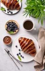 Fresh croissants with chocolate on a white plate on a light background with a blueberries, cup of...