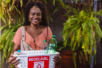 Young black woman, smiling, holding a basket with plastic bottles for recycling.