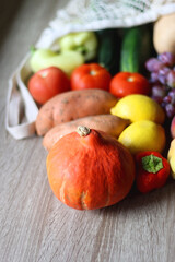 Reusable mesh bag with seasonal fruit and vegetable on wooden background. Late summer or early autumn. Selective focus.
