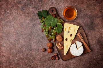 cheese with big holes, emmental, maasdam, brie cheese, on a cutting board, with grapes and honey, nuts, appetizer to wine, top view,