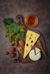 cheese with big holes, emmental, maasdam, brie cheese, on a cutting board, with grapes and honey, nuts, appetizer to wine, top view,