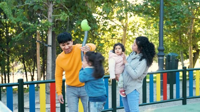 Happy Hispanic parents playing with her children at the synchro spinner in a park. Latin family.