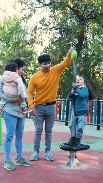 Happy Hispanic parents playing with her children at the synchro spinner in a park. Latin family.