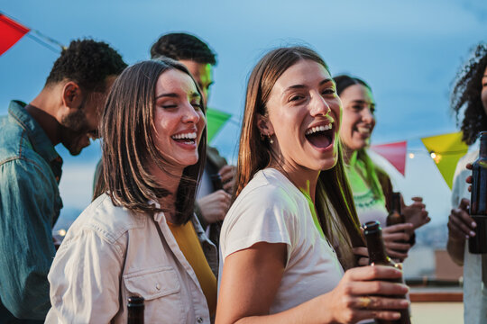 Two excited young adult women dancing together and having fun with friends at music festival. Ecstatic teenage girls celebrating with music on a weekend party. Playful ladies enjoying a birthday event