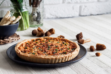 Quiche - open tart pie with morel mushrooms, onion and cheese on a plate - obrazy, fototapety, plakaty