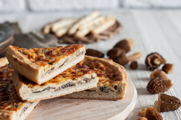 Quiche - open tart pie with morel mushrooms, onion and cheese on wooden cutting board