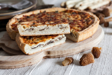 Quiche - open tart pie with morel mushrooms, onion and cheese on wooden cutting board