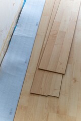 A vertical portrait of a stacked pile of wood imitation laminate floorboards lying on some sound isolation ready to be installed to create a wooden floor in a house on a screed floor.
