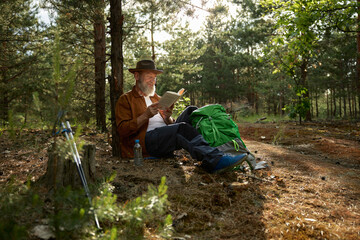 Happy senior man reading funny book during rest after hiking