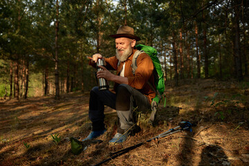 Senior man hiker drinking warm tea from thermos cup in forest