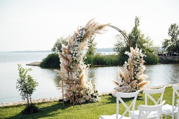 Round arch for a wedding ceremony by the river. White glass chairs stand for guests