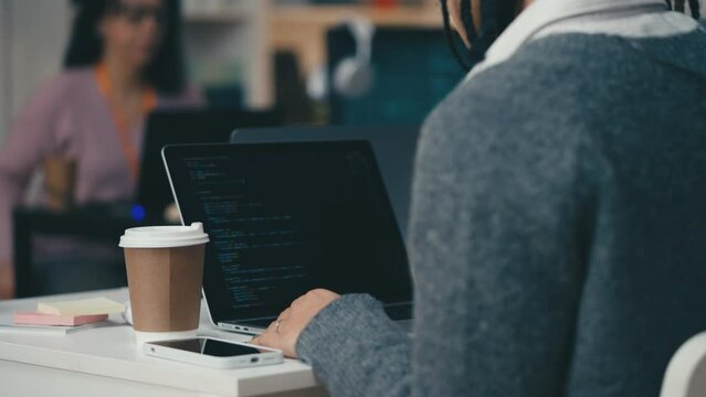 African American female software tester checking code on laptop in office, work
