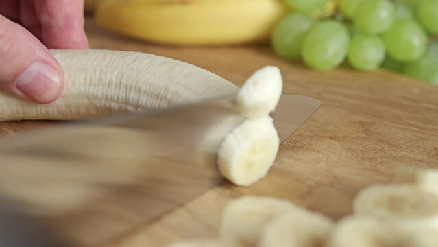 Close-up of male hands cutting fresh banana fruit on a wooden board. Slicing banana fruit.
