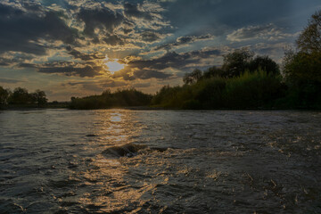 Summer landscape with river flowing water under a magical sunset with the sun shining through the clouds