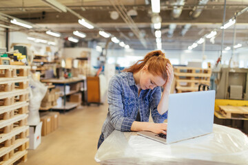 Tired and overworked young woman using the laptop in a warehouse
