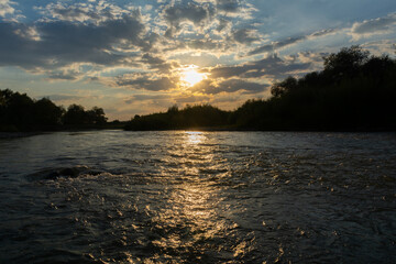 Amazing sunset with sun rays shining through the cloudy sky and a river flowing