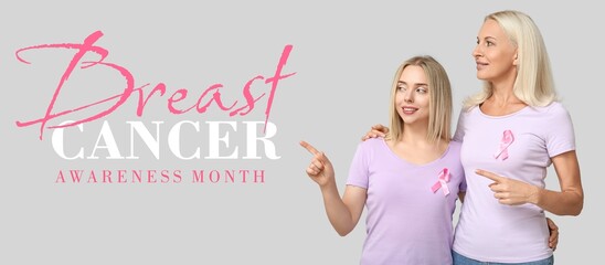 Women with pink ribbons pointing at something on grey background. Breast cancer awareness month
