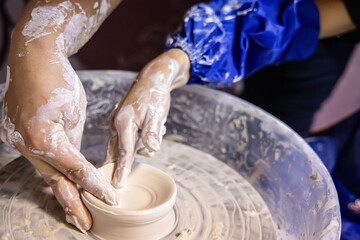The hands of a teacher teaching how to make a plate on a potter's wheel. A child with a teacher in a pottery class