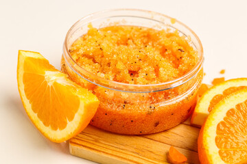Wooden board with jar of natural body scrub and orange slices on light background, closeup