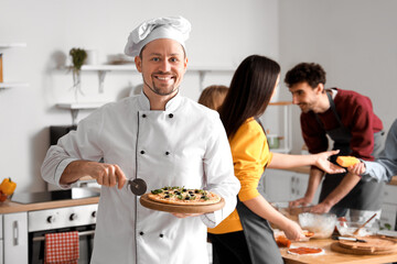 Italian chef with prepared pizza during cooking class in kitchen