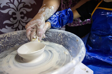 A small child with a teacher while learning the skill of pottery