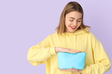 Fototapeta premium Young woman with cosmetic bag on lilac background
