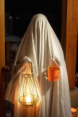 Scary ghost with glowing lantern and halloween candy bucket at doors in spooky atmospheric night....