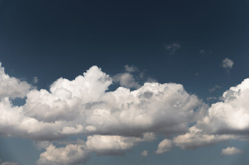 Part of the cloud is divided into large air clouds. White cumulus clouds against clear blue sky close up, cloudy sky background