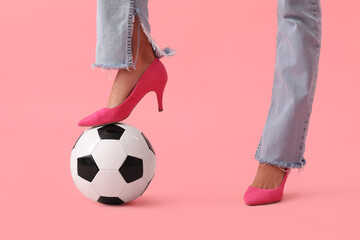 Legs of young woman wearing high heels and playing with soccer ball on pink background