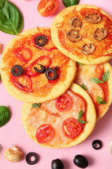 Different tasty mini pizzas and ingredients on pink background