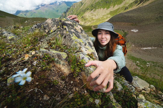 brave young woman fearlessly climbs a steep stone wall in the mountains, overcoming obstacles. Adrenaline and courage in hiking, smiling girl with backpack climbs mountain