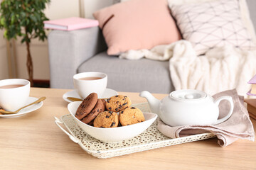 Bowl with cookies, teapot and cups of tea on wooden table in living room