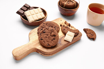 Wooden board with cookies, chocolate and cup of tea on white background