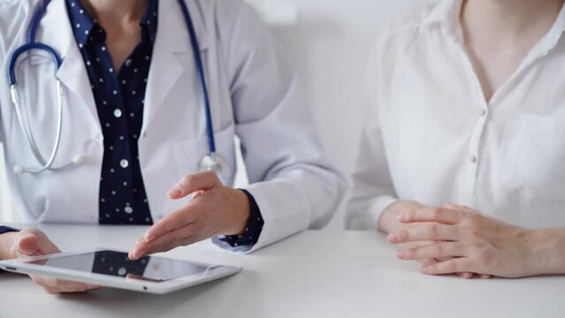 Doctor and patient sitting at the table and talking. The pediatrician in a blue dotted blouse and white medical coat using a tablet PC. Medicine, healthcare concepts