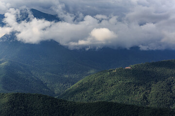 Fototapeta premium Green mountains, big clouds, a small house in the distance. Krasnaya Polyana.
