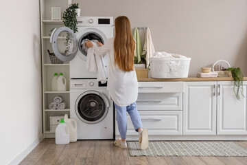 Woman putting dirty clothes into washing machine in laundry room - obrazy, fototapety, plakaty
