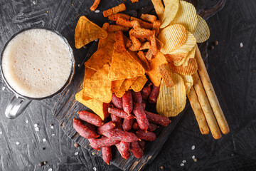 glass of beer, Mini Sausages, Grissini and chips, crackers with Smoked Salami Sticks, vintage wooden cutting board, on a black isolated background