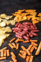 snacks, mini sausages, grissini and chips, crackers with smoked salami sticks, on a black isolated background